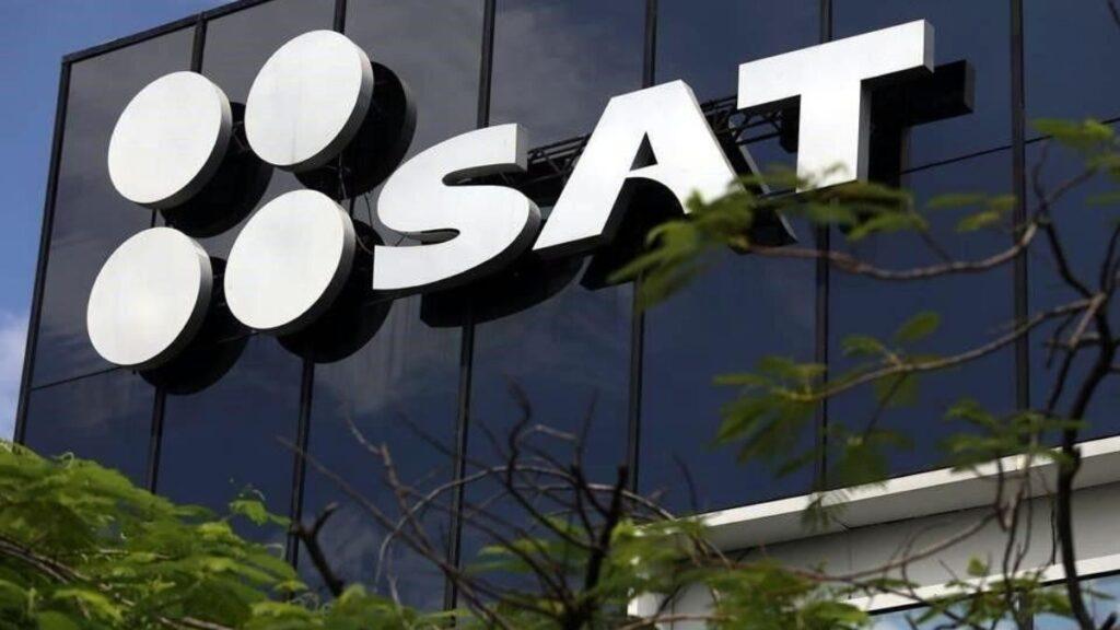Sat-acorrala-a-samuel-garcía-deuda-nuevo-león - Tu Vecino Informa Osat Logo on a Dark Glass Office Building with Tree Branches in the Foreground. - Tu Vecino Informa