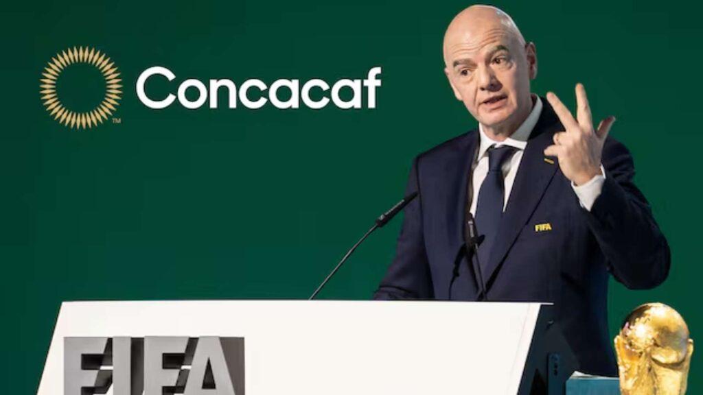 Man in Suit Speaking at a Podium with a Concacaf Backdrop and Microphone on Teal/green Background. - Tu Vecino Informa