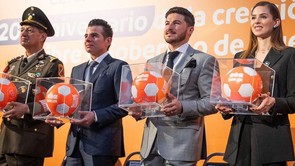 Tu-vecino-informa-samuel-garcia-sepulveda-nljpg - Tu Vecino Informa Four People in Suits Plus a Military Officer Stand in a Row, Each Holding a Clear Box Containing an Orange-and-white Soccer Ball at a Formal Ceremony. - Tu Vecino Informa
